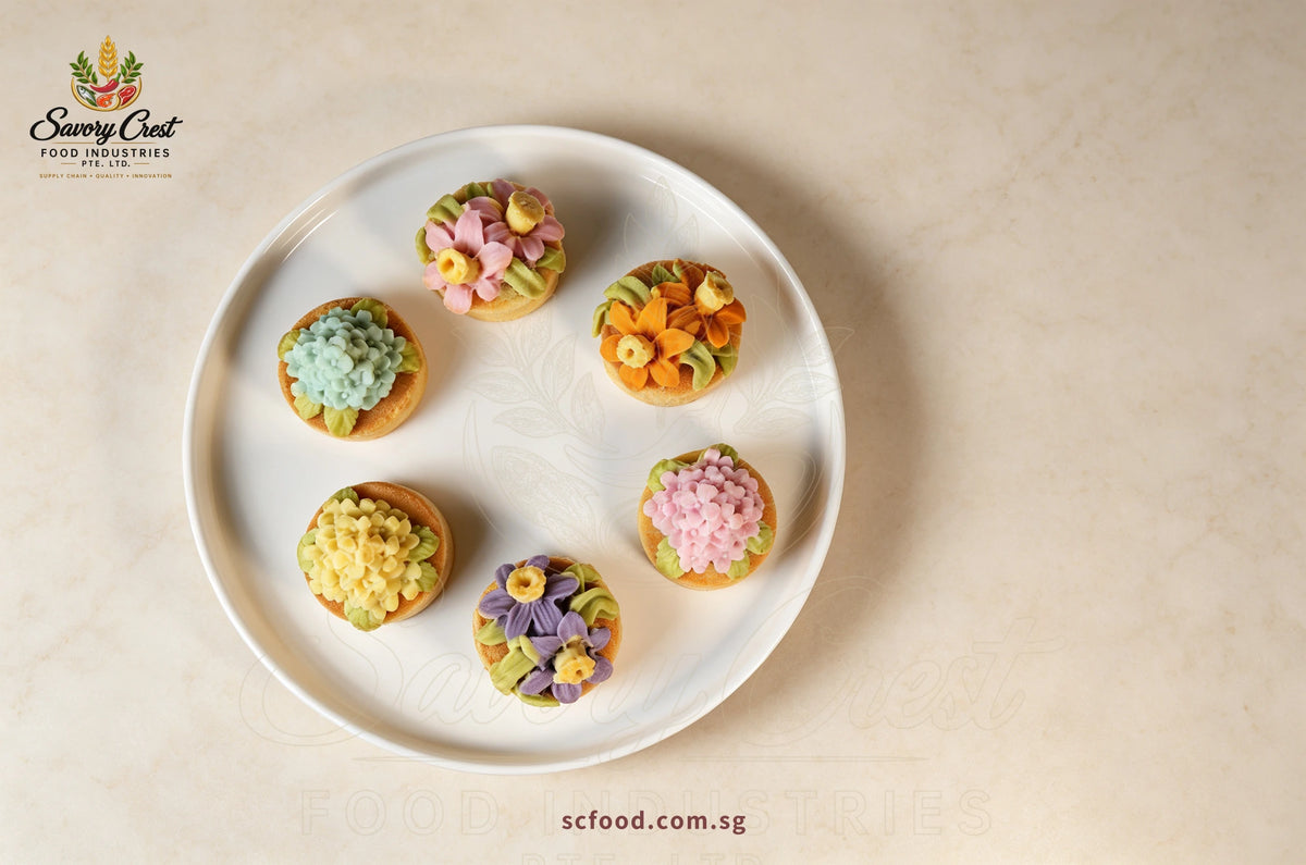 Six flower-shaped pastries in pink, orange, purple, yellow and pale blue-green arranged on a white plate.