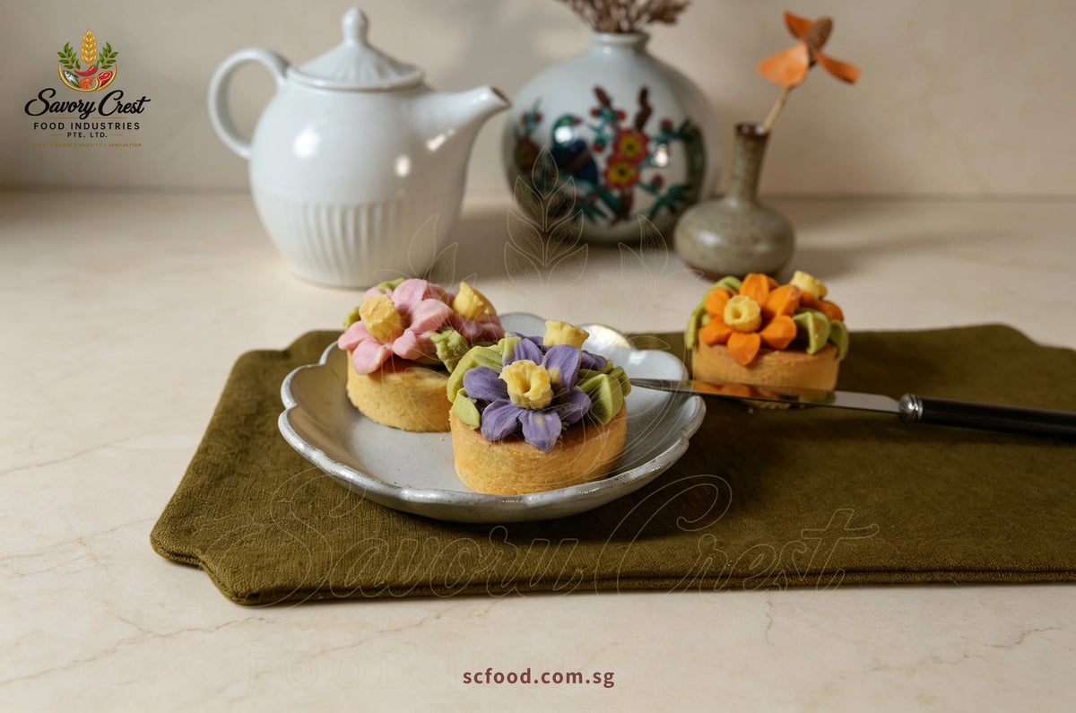 Pink, purple and orange floral pastries beside a white teapot on an olive-green table mat.