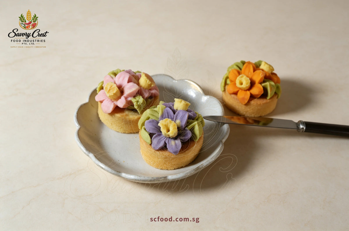 Close-up of pink and purple floral pastries on a scalloped plate, with an orange floral pastry alongside.